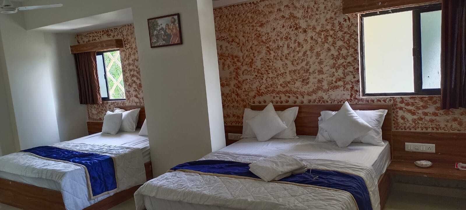 A room with two beds, floral wallpaper, a window with curtains, and a painting on the wall.