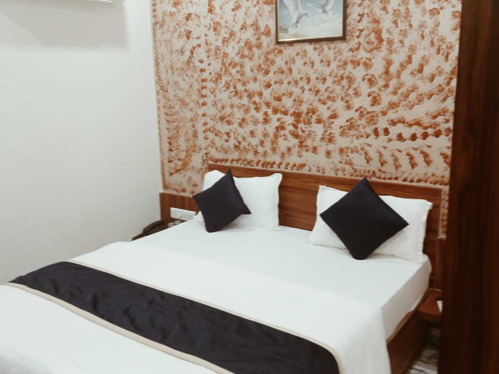 Una cama bien tendida con ropa de cama blanca y negra, un cabecero de madera y un papel tapiz con estampado floral detrás.
