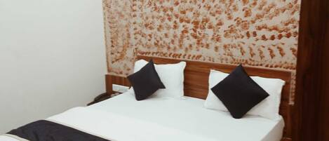 Una cama bien tendida con ropa de cama blanca y negra, un cabecero de madera y un papel tapiz con estampado floral detrás.
