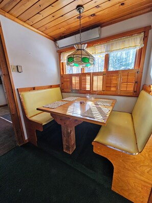 A wooden dining area with a table, chairs, and a window with shutters. - J&D Hand Crafted Cabin (Russell)