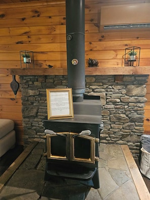 A wood-burning stove with a stone fireplace, a framed sign, and a wooden bench. - J&D Hand Crafted Cabin (Russell)