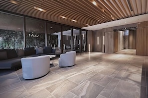 A spacious lobby with a modern design, featuring a large seating area with sofas and armchairs, a tiled floor, and large windows allowing natural light.