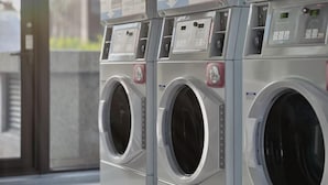 A row of industrial-style, stainless steel front-loading washing machines with control panels and instructional signs. - Boutech Jiantan Hotel (Taipei)