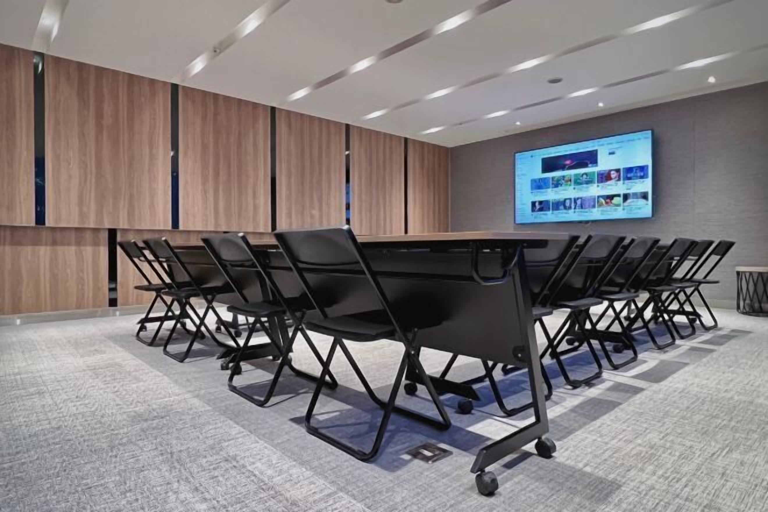 A conference room with a long table, black chairs, a large screen, and wooden paneling on the walls.