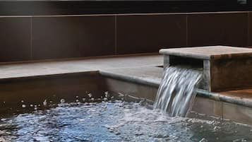 Ein Wasserspiel mit einem kaskadenartigen Wasserfall in ein rechteckiges Becken, vor einer mit Fliesen verkleideten Wand.
