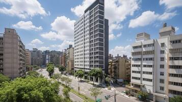 Um edifício alto com design moderno, cercado por outros edifícios e um céu claro.