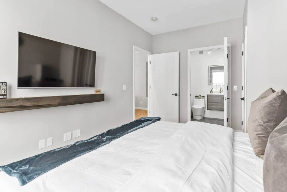 A modern bedroom with a large bed, a mounted TV, and a bathroom visible through an open door.