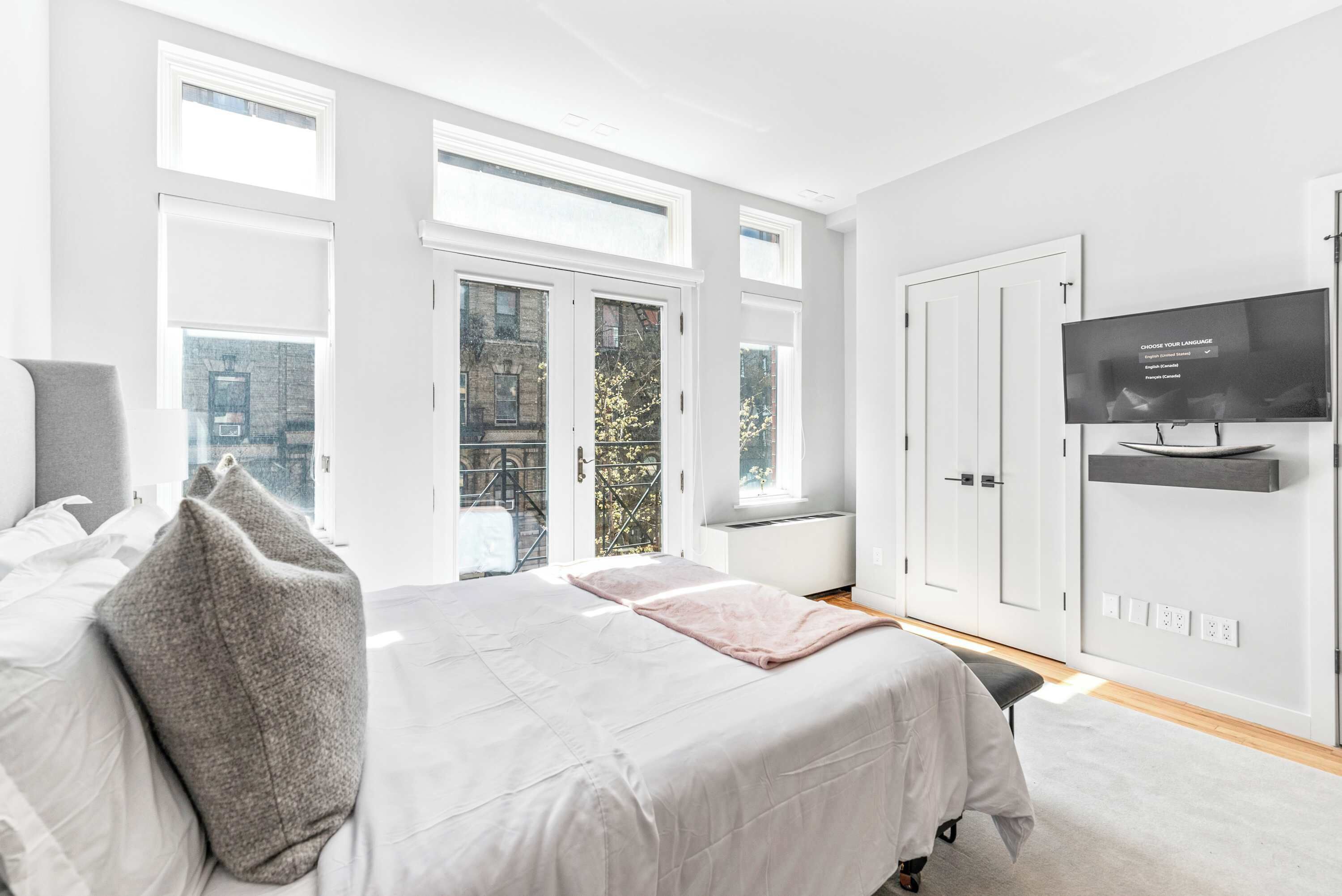 A modern bedroom with a large bed, a television, and a balcony with a view of the city.