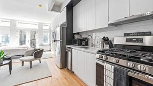 A modern kitchen with stainless steel appliances, a dining area with a sofa and table, and large windows providing natural light. - Luxe Studio with Charming Juliet Balcony (New York)