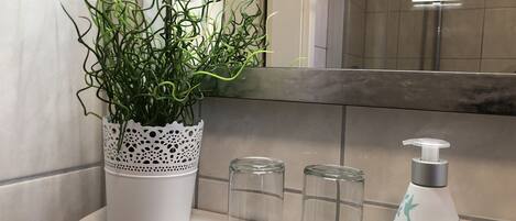A bathroom with a white sink, a potted plant, two clear glass bottles, and a white soap dispenser with a bird design.