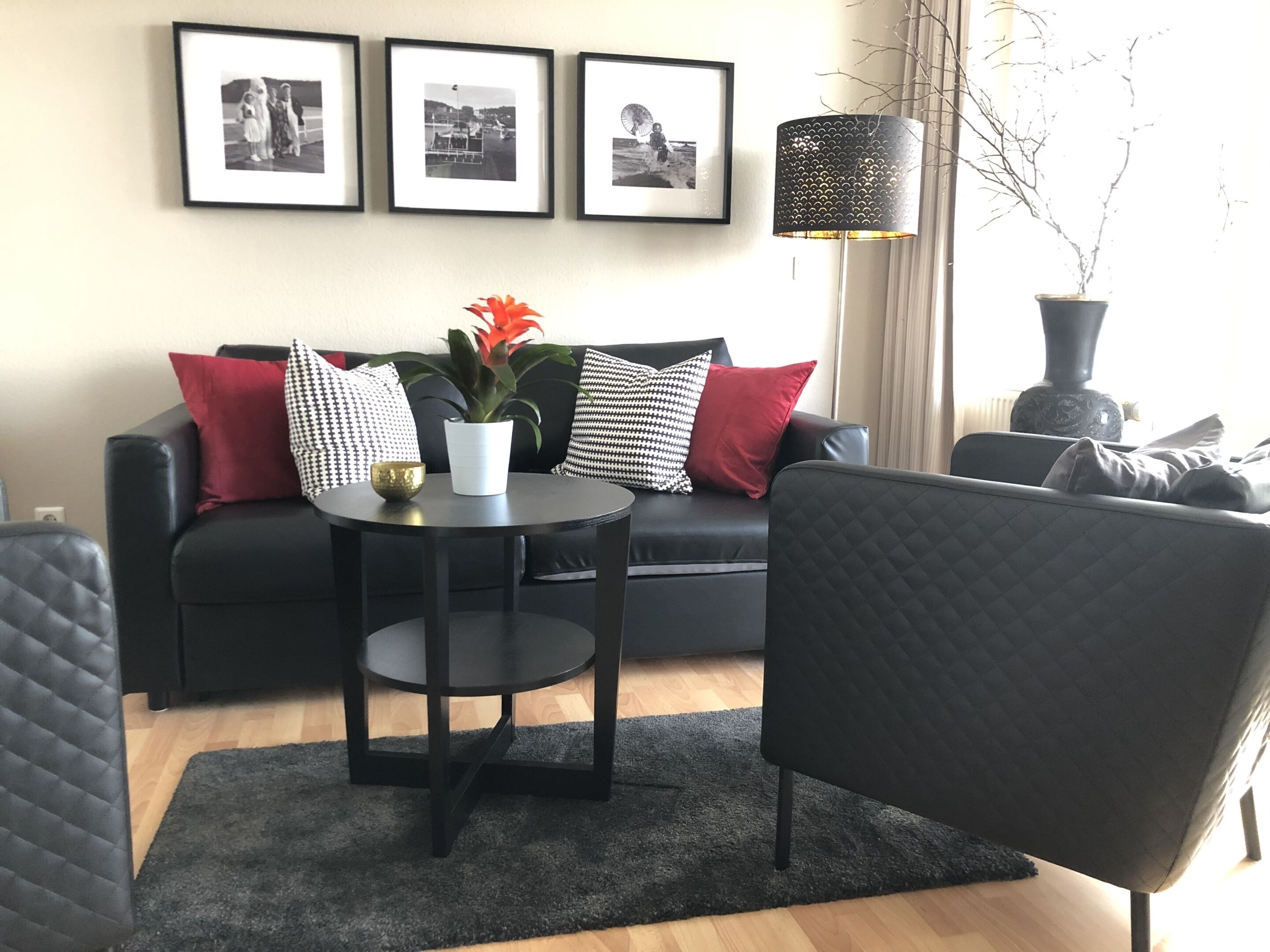 Ett modernt vardagsrum med en svart soffa, ett runt svart bord med en krukväxt och tre inramade svartvita fotografier på väggen.