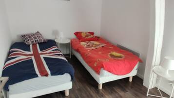 Un dormitorio con dos camas individuales, una mesita de noche pequeña, una lámpara blanca y un cuadro en la pared.