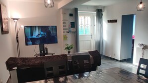 Ruokailutila, jossa on suuri pöytä, tuoleja, televisio ja riippuvalaisimet.