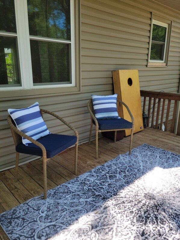 A wooden deck with two wicker chairs, each with a blue cushion and a striped pillow. A patterned rug is laid out on the deck. - Come relax in our lovely home within walking distance to the Masters. (Augusta)