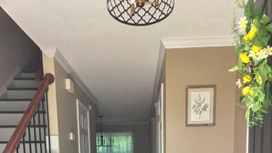 Ein Flur mit einer Holztreppe, einem Blumentopf, einer gerahmten Pflanzenillustration und einer Tür mit schwarzem Griff.