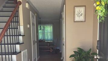 Un couloir avec un escalier en bois, une plante en pot, une illustration botanique encadrée et une porte dotée d’une poignée noire.