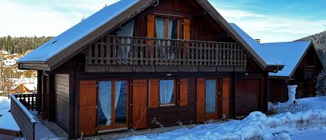 Un chalet in legno con un balcone, ampie finestre e un tetto innevato.