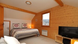 Une chambre à coucher avec un lit, un téléviseur posé sur un meuble en bois, une fenêtre donnant sur un paysage et une porte.
