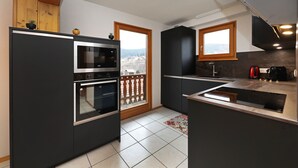 Une cuisine moderne dotée d’un four encastré, d’un micro-ondes et d’une grande fenêtre donnant sur un balcon.