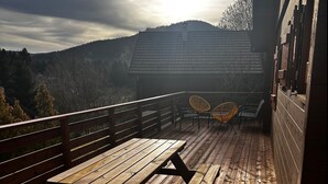Une terrasse en bois avec une table de pique-nique et deux chaises en osier.