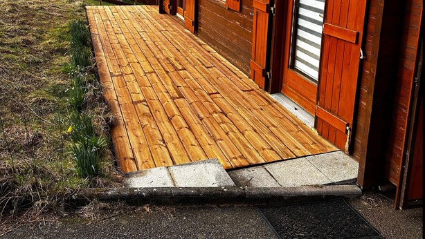 Un bâtiment en bois doté d’une terrasse en bois qui mène à un ensemble de portes en bois.
