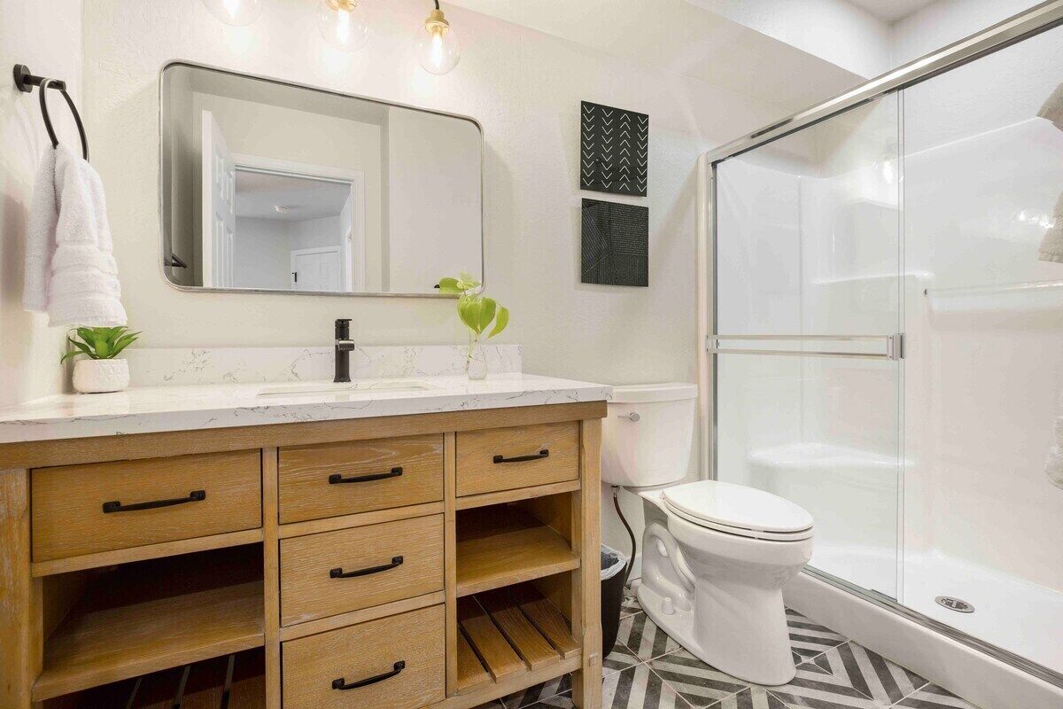 Une salle de bain moderne avec un meuble-lavabo en bois, un grand miroir, des toilettes blanches et une douche à parois de verre.