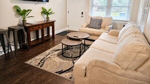 Un salon avec un canapé, une table basse, un téléviseur et deux plantes en pot.