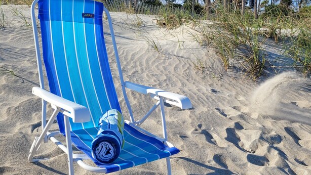 Une chaise de plage recouverte d’une housse à rayures bleues et blanches, sur une plage de sable.