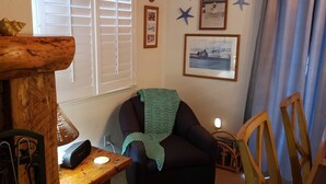 Ett mysigt rum med ett träbord, en stol med en grön filt, en lampa och inramade bilder på väggen.