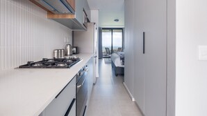 A modern kitchen with a gas stove, oven, and microwave, leading to a bedroom with a bed and a view of the sea. - Cosy Studio - Umhlanga Ridge - Pool - Aircon - Gym (Cape Town)