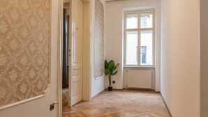 Ein Flur mit strukturiertem Wandpapier, Holzdielen, einer Heizung und einem Fenster mit Blick.