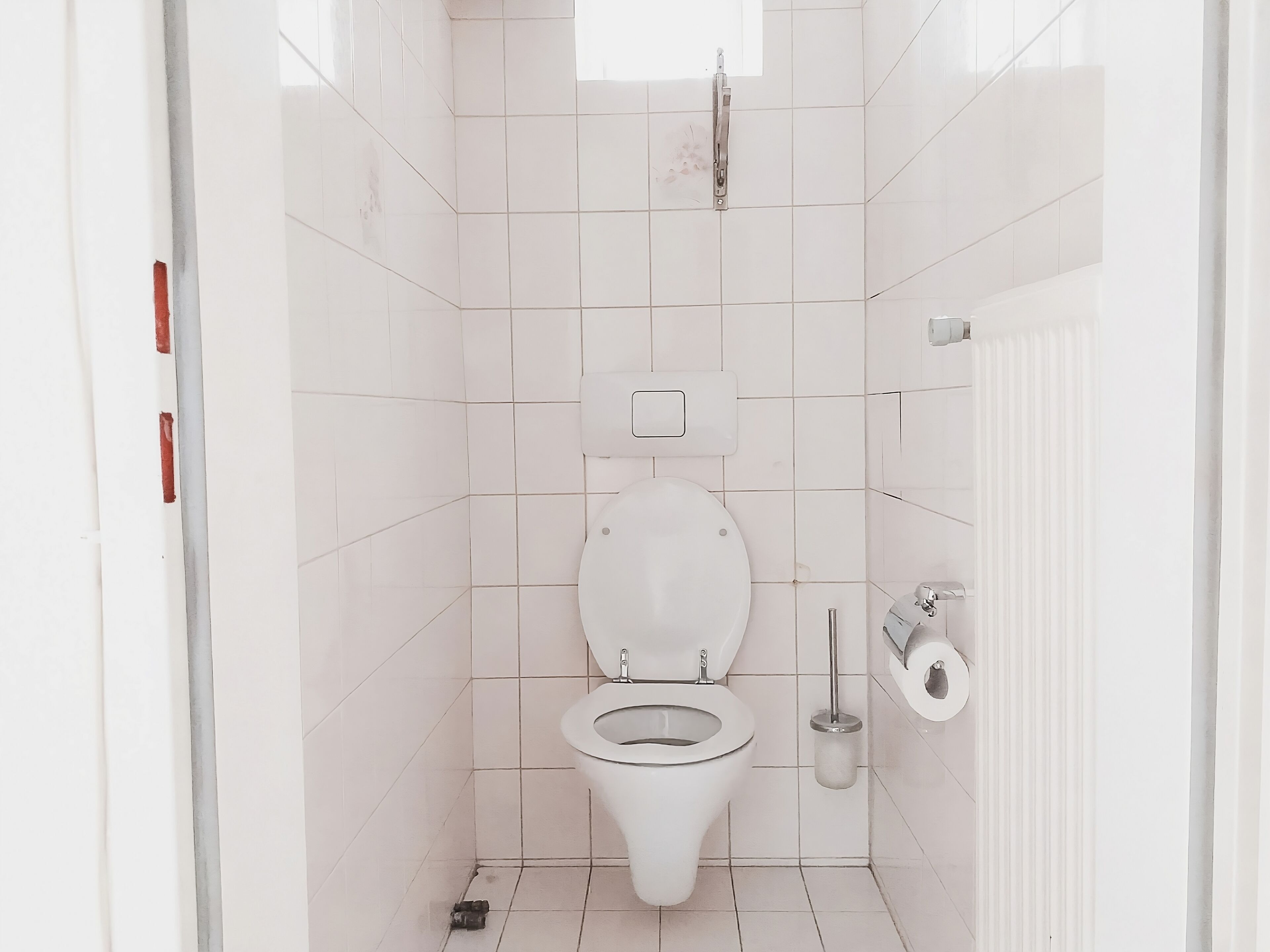 A small, modern bathroom with white tiles, a toilet, a bidet, and a toilet paper holder.