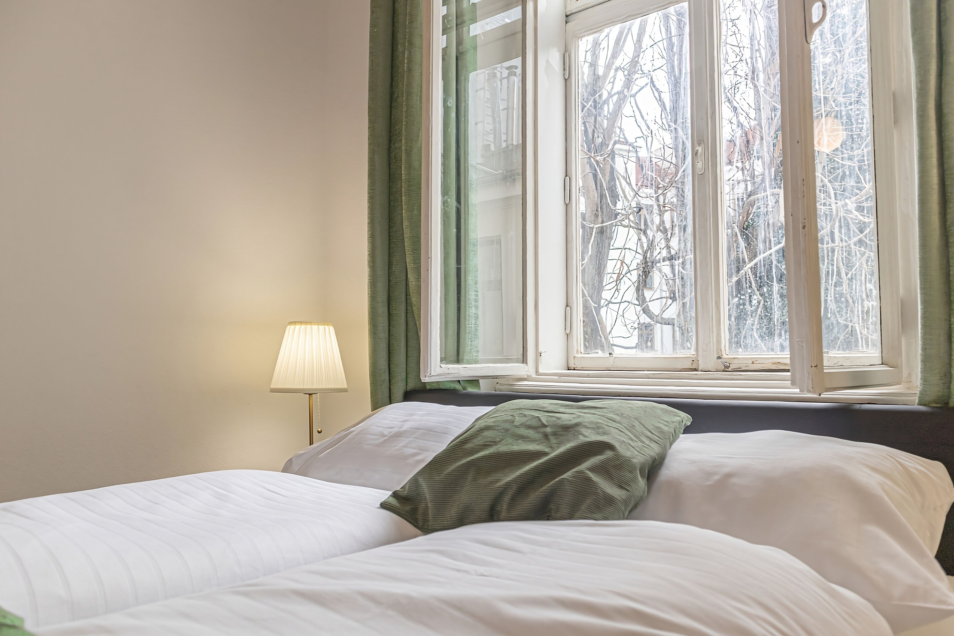 Un dormitorio con cama, lámpara y ventana con vistas a árboles.