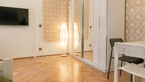 Ein modernes Zimmer mit einem wandmontierten Flachbildfernseher, einem großen Spiegel und einem Essbereich mit weißem Tisch und Stühlen.