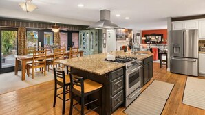 A modern kitchen with a central island, stainless steel appliances, and a dining area with wooden chairs.