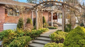 A residential property with a brick exterior, a wooden pergola, and a well-maintained garden with steps leading to the entrance.