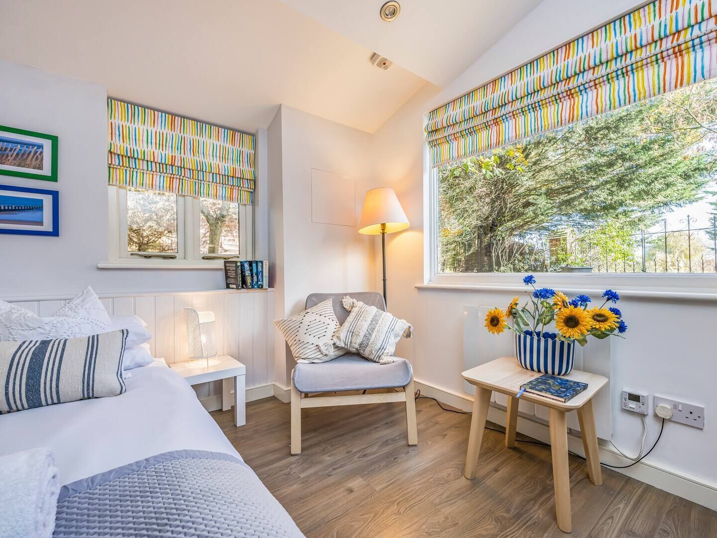 A bedroom with a bed, a chair, a bedside table with a lamp, a window with curtains, and a vase with flowers.