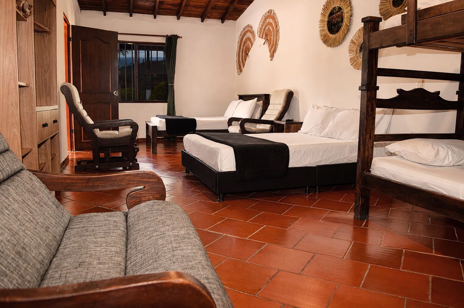 A room with a bed, two chairs, a sofa, and a wooden wardrobe.
