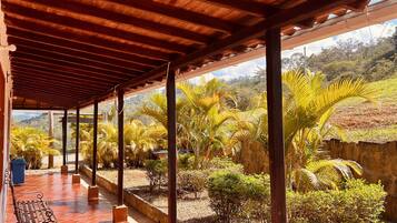 A covered outdoor area with tiled flooring, wooden beams, and a bench.