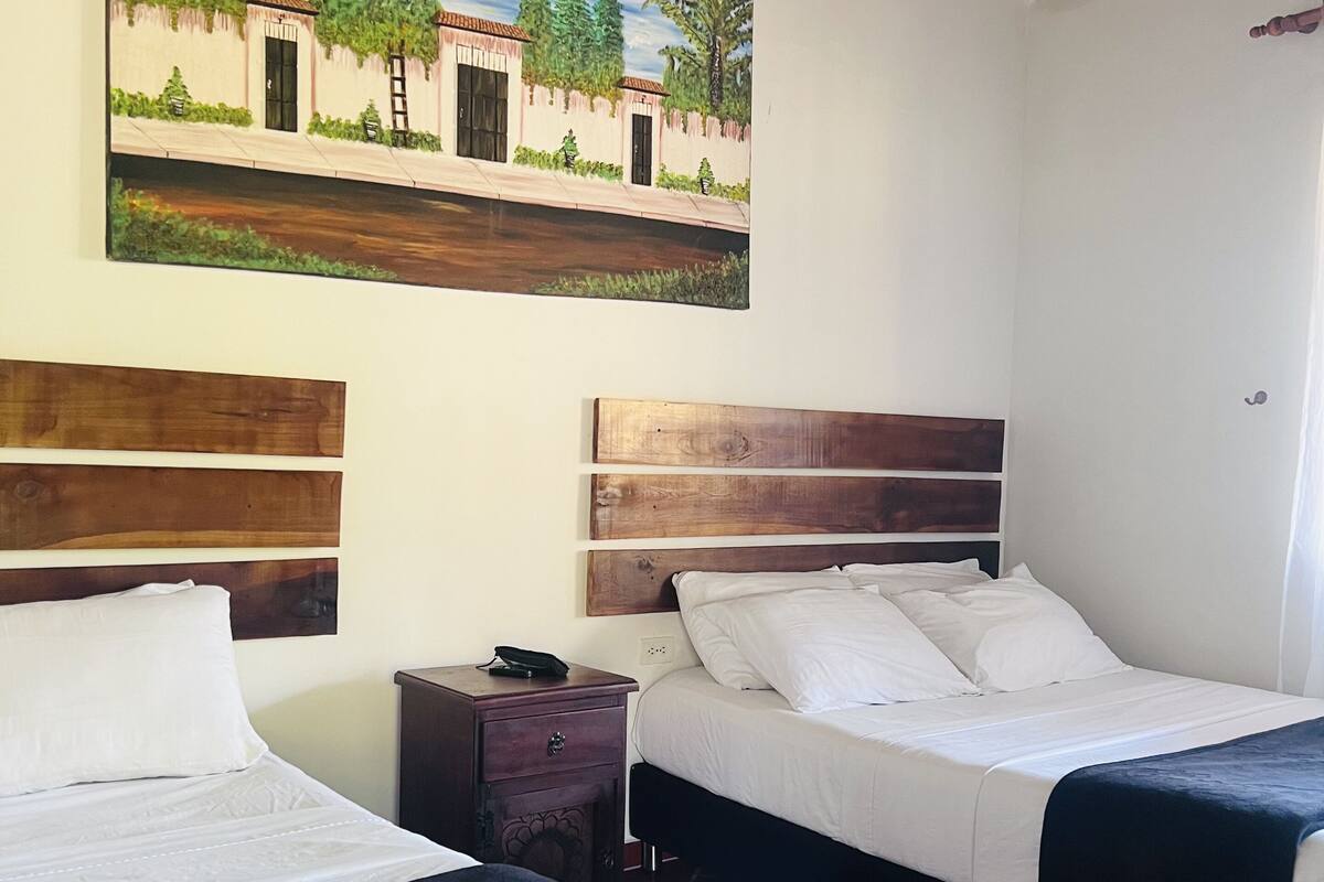 Ein Hotelzimmer mit zwei Betten, Holz-Kopfteilen, einem Nachttisch und einem Gemälde eines Gebäudes an der Wand.