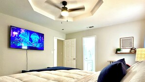 Een slaapkamer met een bed, een plafondventilator, een televisie aan de muur en een deur naar een andere kamer.