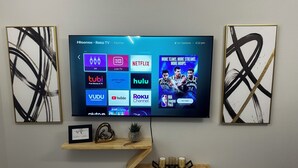 Een flatscreen televisie bevestigd aan een muur, met daaronder een houten plank waarop decoratieve objecten staan.