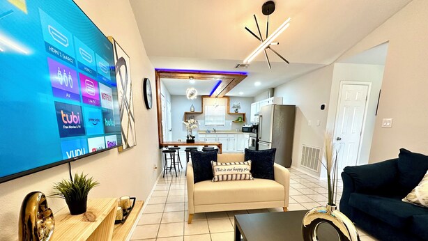 Een moderne woonkamer met een flatscreen televisie, een bank, een salontafel en een eethoek op de achtergrond.