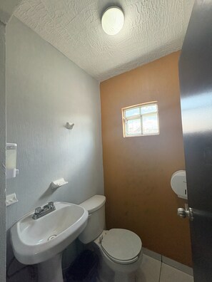 A bathroom with a toilet, sink, and a small window. - Casa Loma Dorada Residencial B (Tonalá)