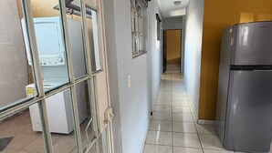 Ένας διάδρομος με μια μικρή κουζίνα, η οποία περιλαμβάνει ένα ψυγείο, ένα πλυντήριο ρούχων και ένα παράθυρο με μεταλλικό πλαίσιο.