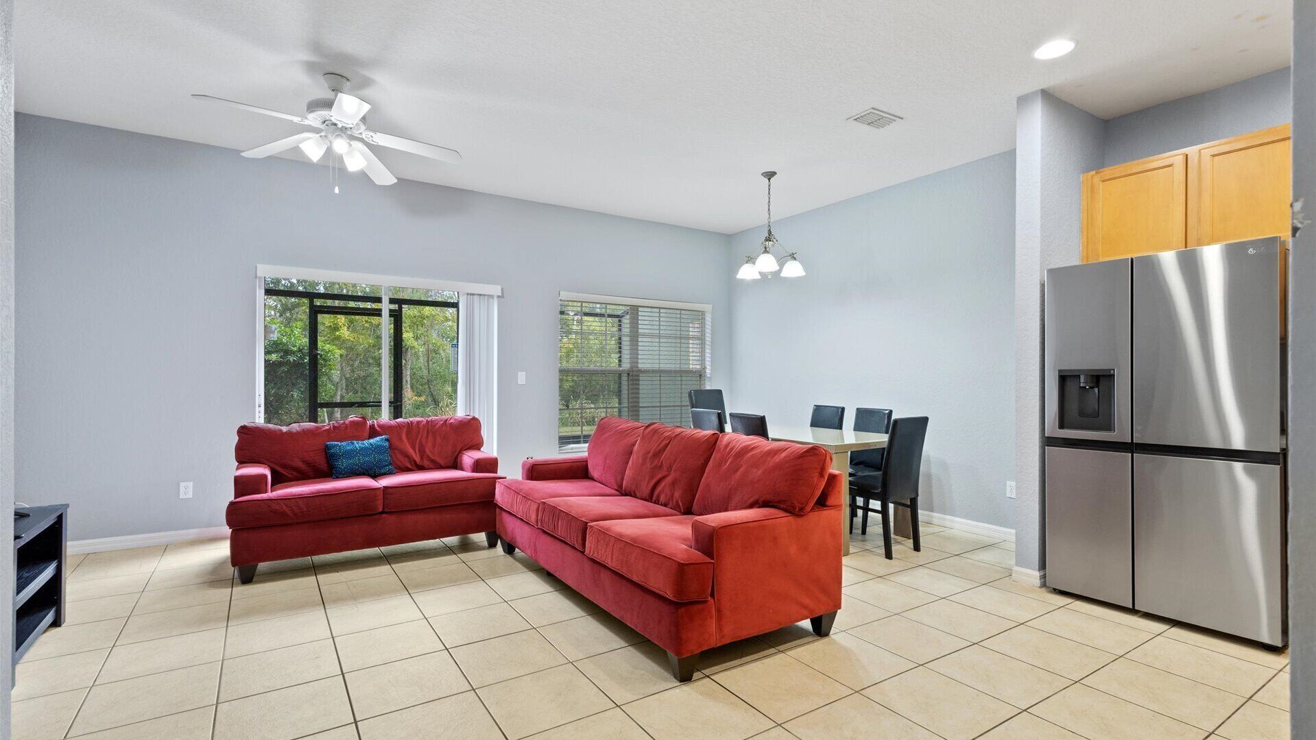 A modern living room with a red sectional sofa, a dining area with a table and chairs, and a kitchen with a stainless steel refrigerator.