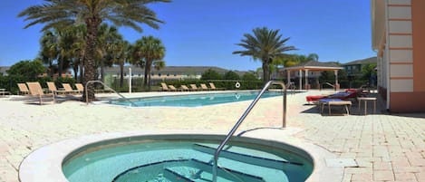 A swimming pool with a hot tub, surrounded by lounge chairs and palm trees.