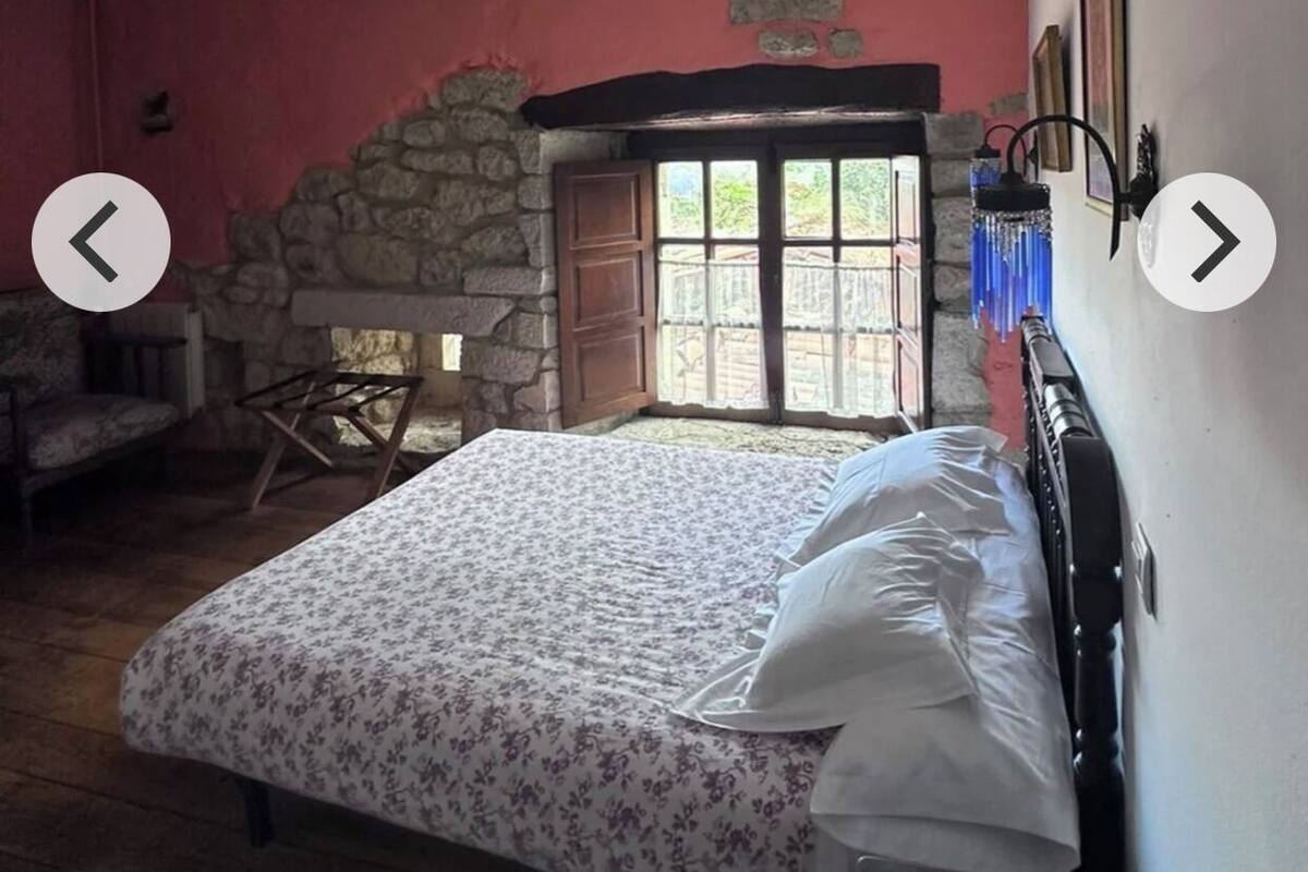 Une chambre à coucher avec un lit, une cheminée en pierre, une fenêtre et un fauteuil.