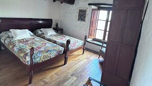 A bedroom with two wooden beds, a wooden wardrobe, and a window with a view.