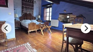 A bedroom with a wooden bed, a small table, a chair, a window, and a patterned rug.